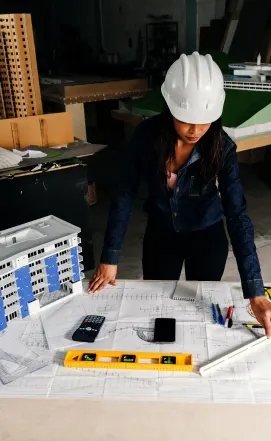 A female architect in a hard hat reviewing blueprints, showcasing project-based Procurement Services in California for the construction and development industries.