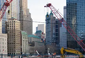 Red construction cranes operating amidst high-rise Manhattan buildings, highlighting industrial procurement consulting firms in New York.