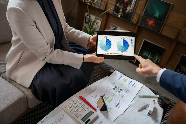 A professional presenting a digital Project Procurement Management Plan on a tablet during a business meeting, featuring detailed data charts and a physical procurement lifecycle diagram on the table.